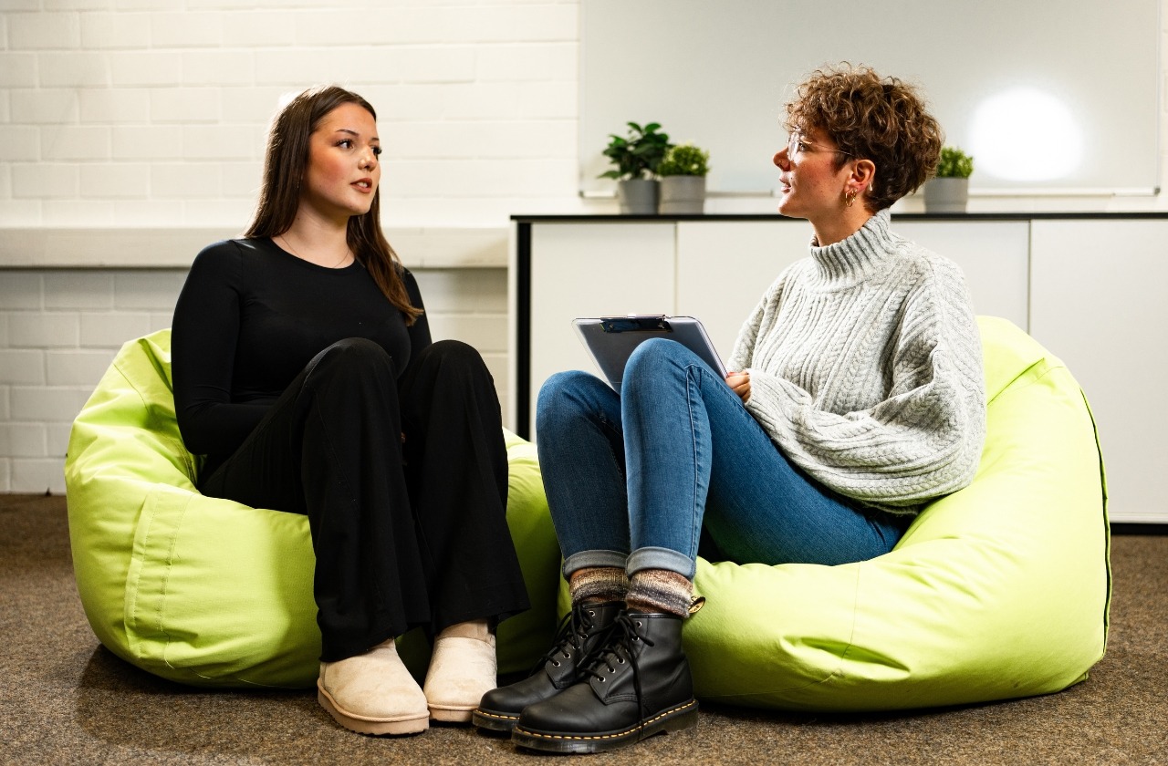 Zwei Frauen sitzen auf grünen Sitzsäcken und führen ein Gespräch, eine hält ein Klemmbrett in der Hand
