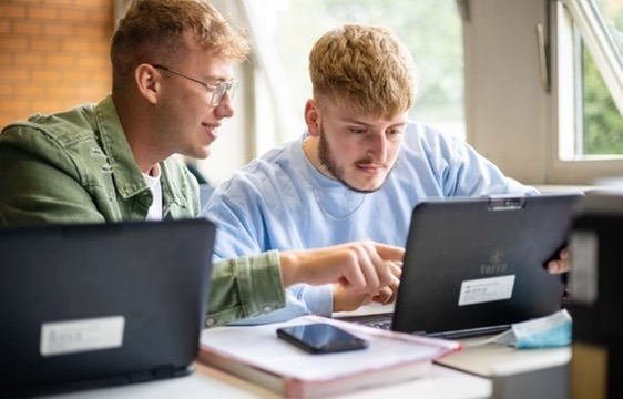 Zwei Studierende arbeiten gemeinsam an einem Laptop in einem Seminarraum
