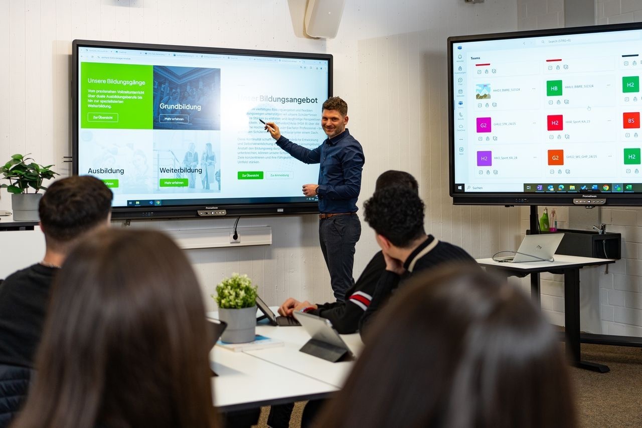 Lehrender präsentiert Bildungsangebote auf einem interaktiven Display vor Schülerinnen und Schülern im Klassenraum