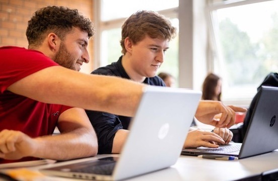 Zwei Studierende arbeiten gemeinsam an einem Laptop in einem Seminarraum