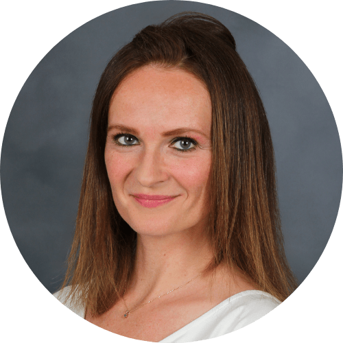 Porträtfoto einer lächelnden Frau mit langen braunen Haaren vor grauem Hintergrund