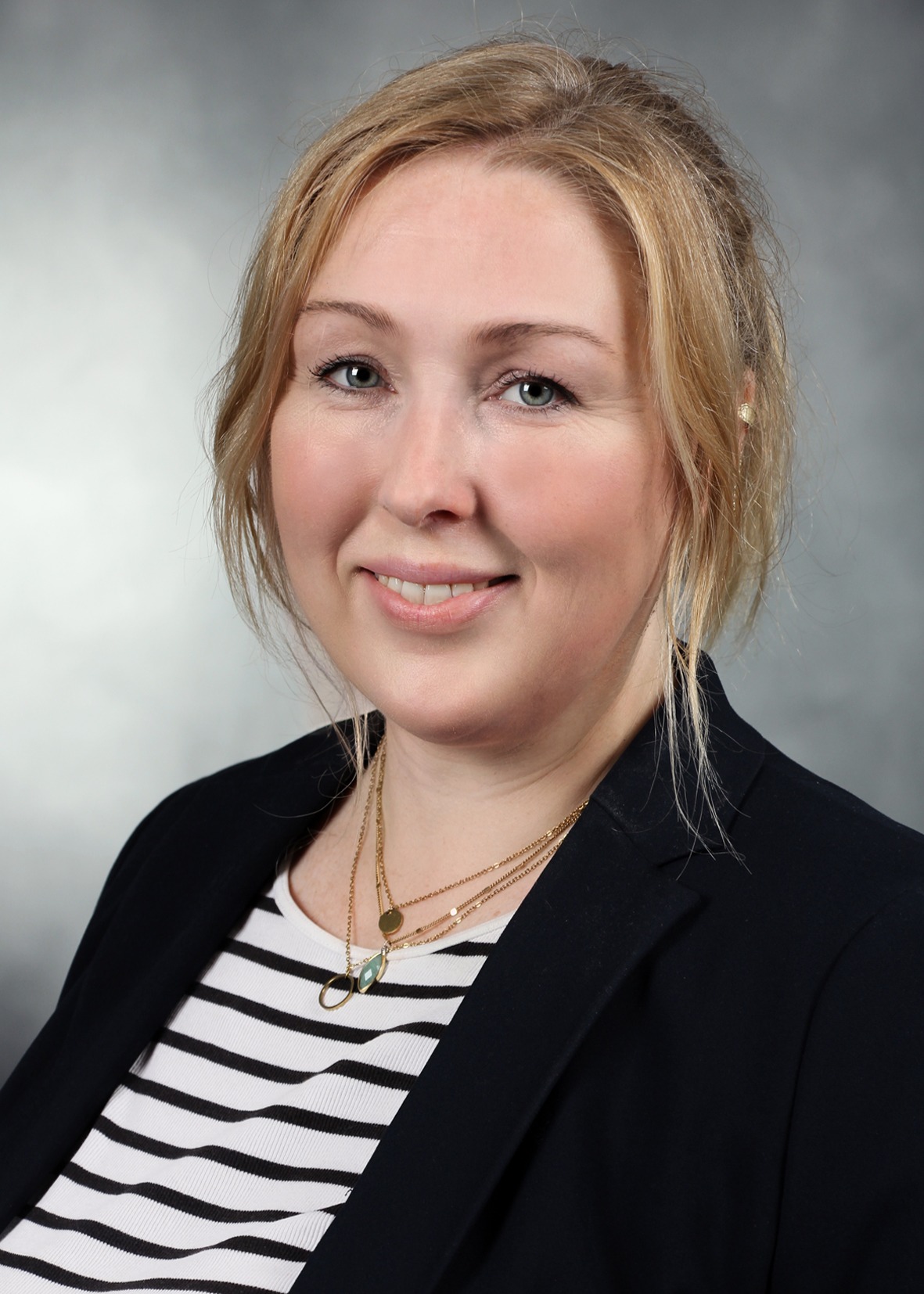 Porträtfoto einer lächelnden Frau mit blondem Haar, schwarzem Blazer und gestreiftem Oberteil