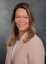 Professionelles Porträtfoto einer lächelnden Frau in einem hellrosa Blazer vor grauem Hintergrund